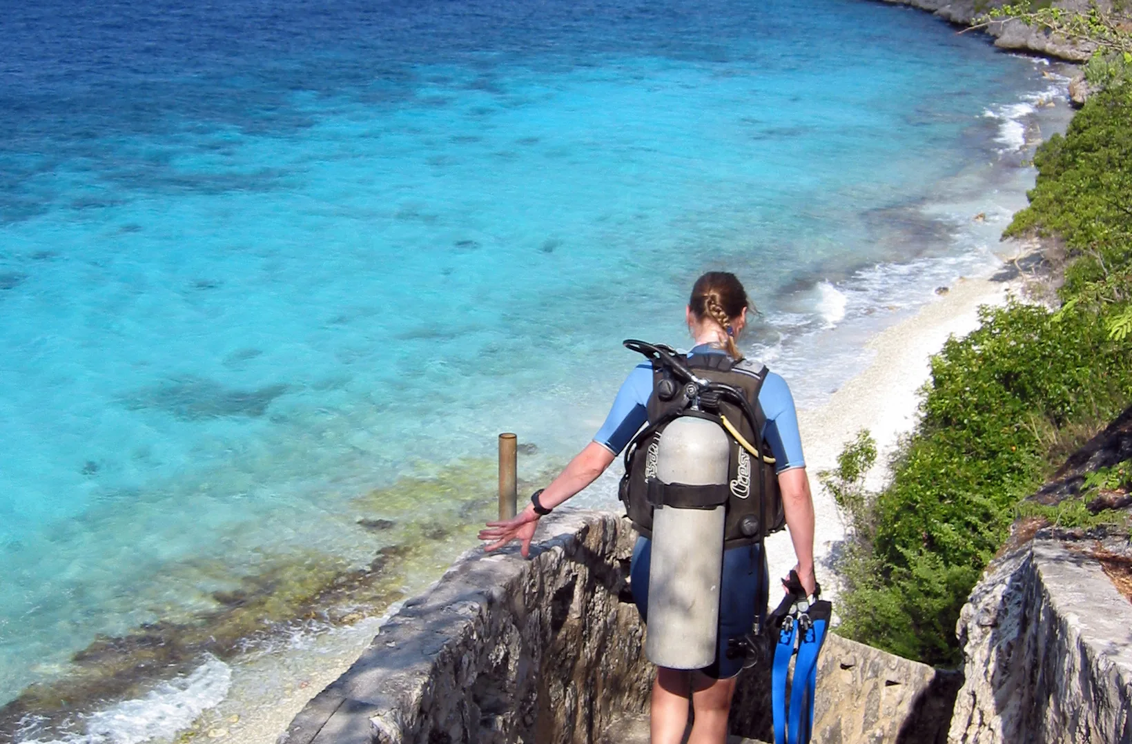 Duiker met fles en flippers daalt af naar het water langs een rotsige kustpad op Bonaire