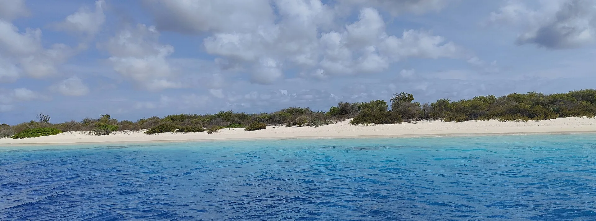 Klein Bonaire gezien vanuit het water met laag begroeid eiland en witte zandstrook aan de kust
