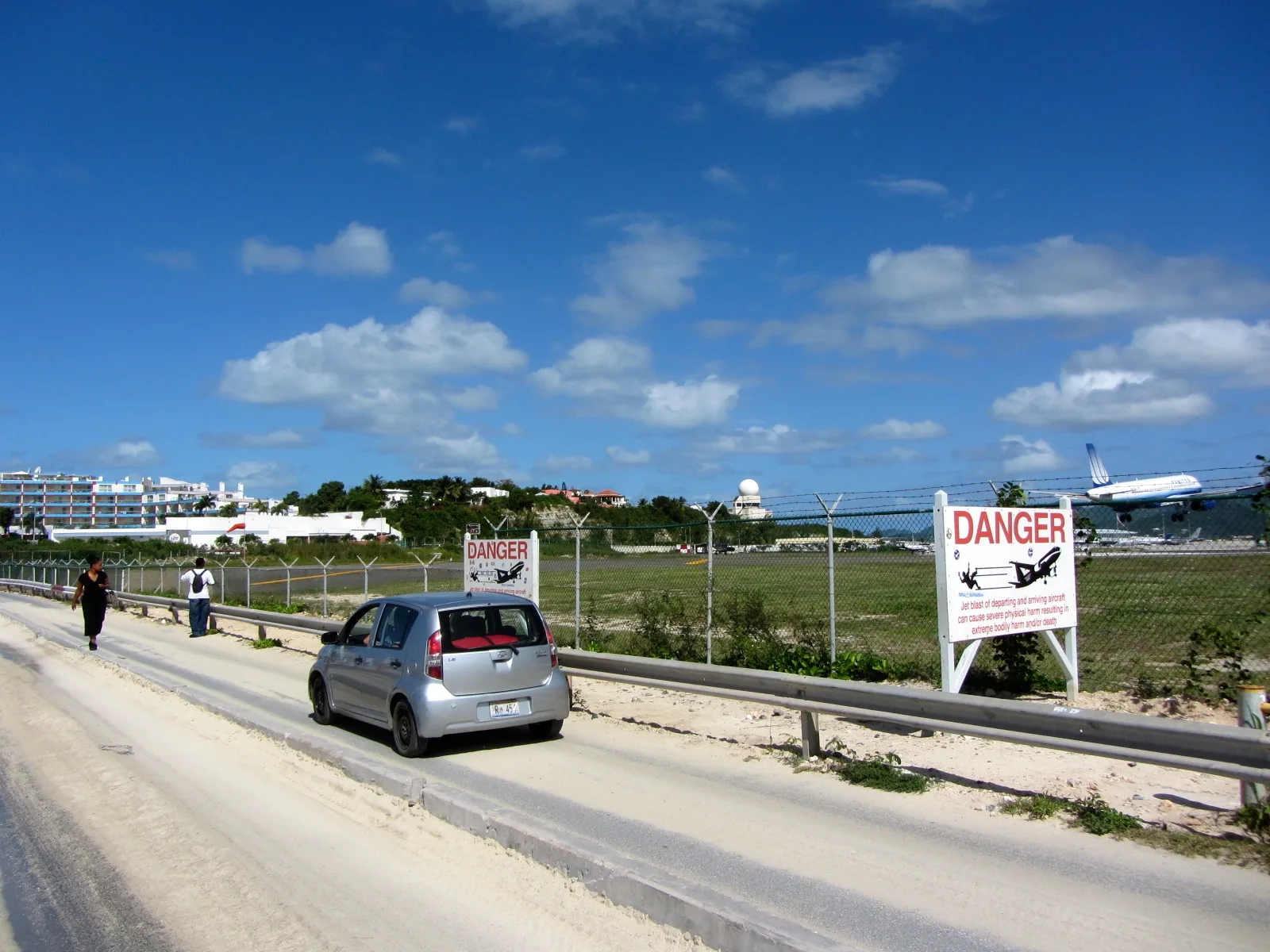 Landend vliegtuig op lage hoogte boven de smalle zandstrook van Maho Beach op Sint Maarten, badgasten op de voorgrond