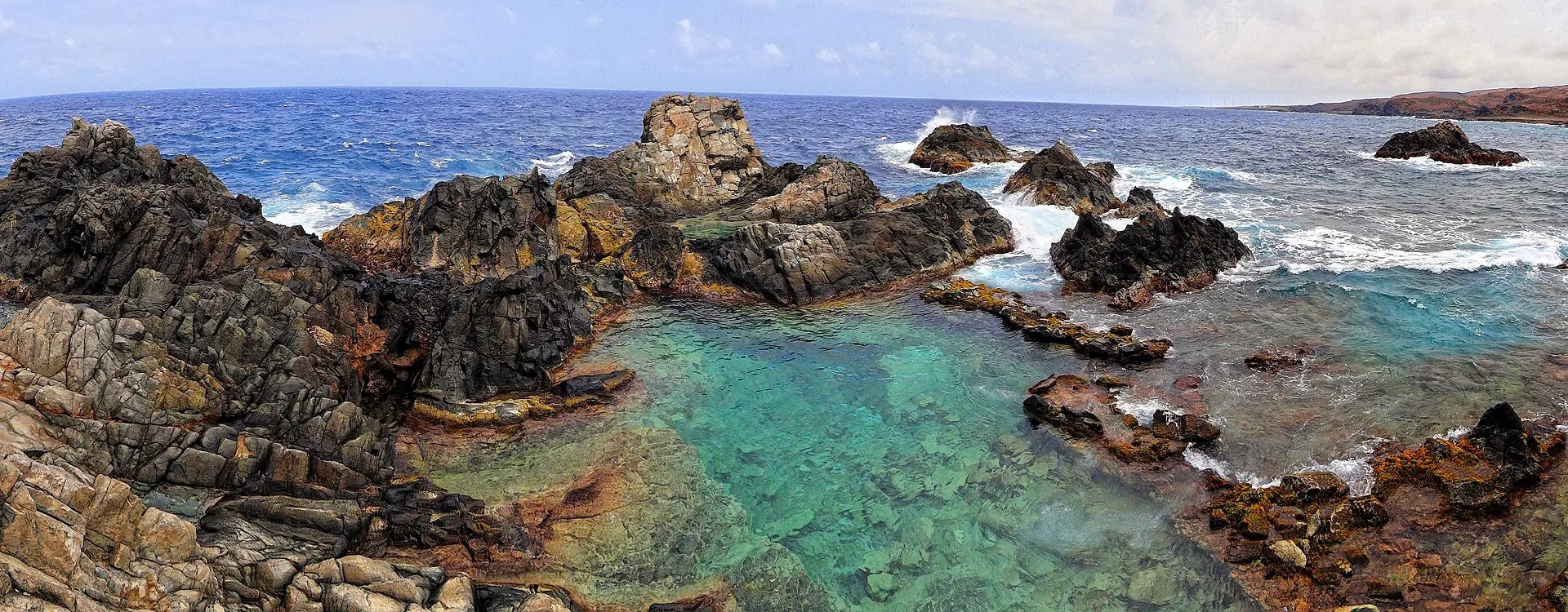 De Natural Pool (Conchi) op Aruba: een ronde rotspool gevuld met helder zeewater, omringd door zwarte lavastenen